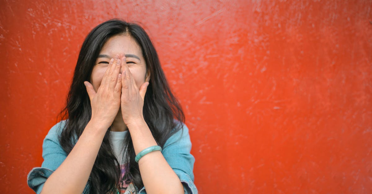 Have any other real people appeared in The Good Place? - Young overjoyed Asian female in casual outfit covering face with hands and laughing while standing against vibrant orange wall