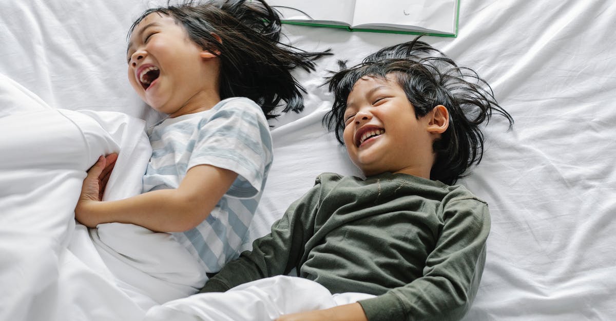 Have the differences of the movie's ending from the book ever been explained? - From above of Asian boy and girl laughing and smiling while lying in sleepwear on bed in morning n bedroom