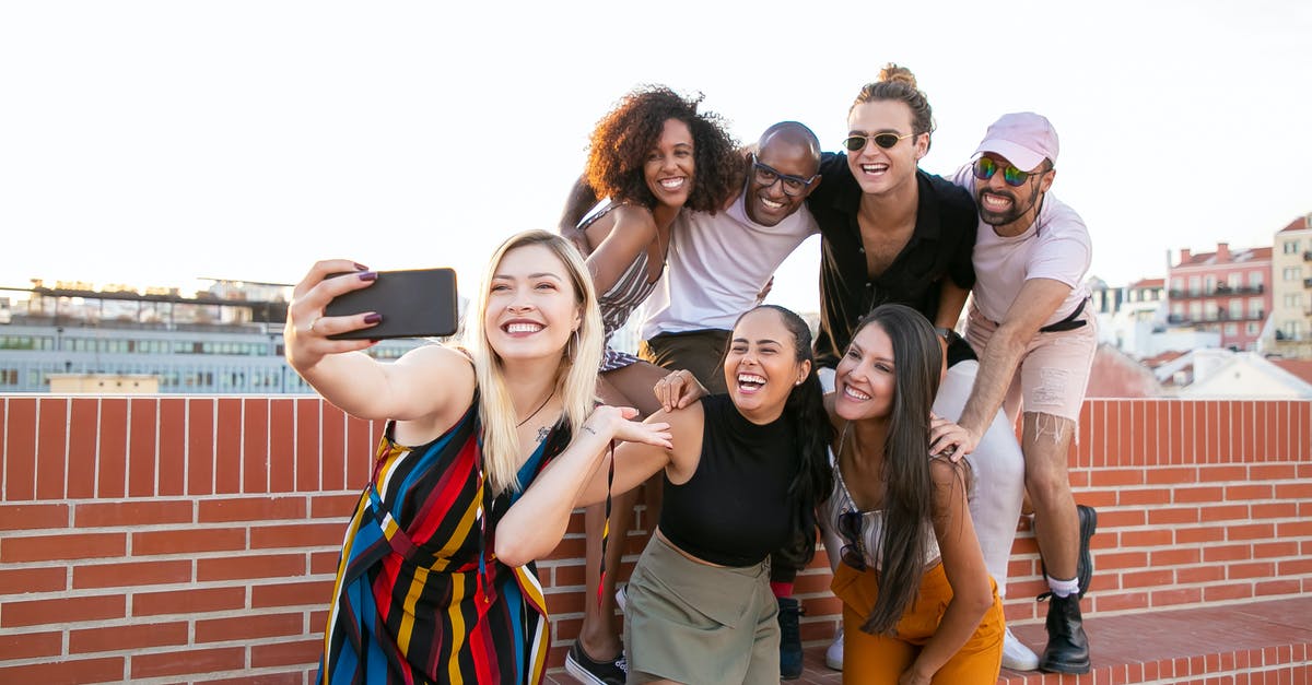 How are they captured? - Group of cheerful young male and female multiracial friends laughing and taking selfie on smartphone while spending time together on terrace