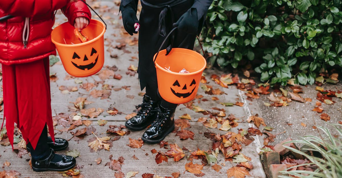 How can a witch/wizard disguise themselves, excluding Polyjuice Potion? - Crop unrecognizable kids in red devil costume with pitchfork and in black witch costume on Halloween with buckets full of candies standing on road in autumn day