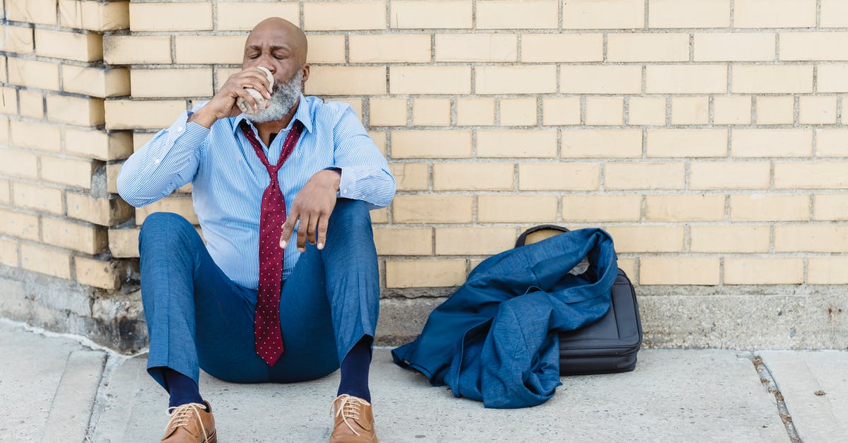 How can alien in human suit cry? - Full body of mature African American bearded businessman in blue trousers and light shirt with maroon tie sitting on ground at brick wall and drinking beverage from tin can