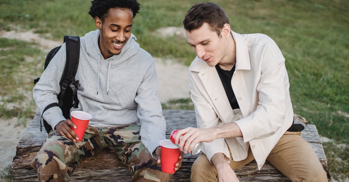 How can Jacoby be with Lana and Ben at the same time? - High angle of male pouring carbonated drink from tin can to smiling black friend sitting with red cup