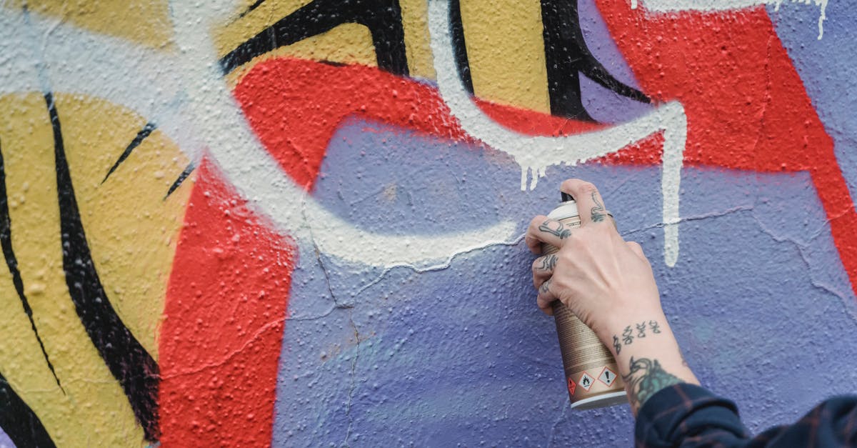 How can Malekith create the Aether? - Hand of crop anonymous tattooed person spraying white paint from can on colorful wall while standing on street of city