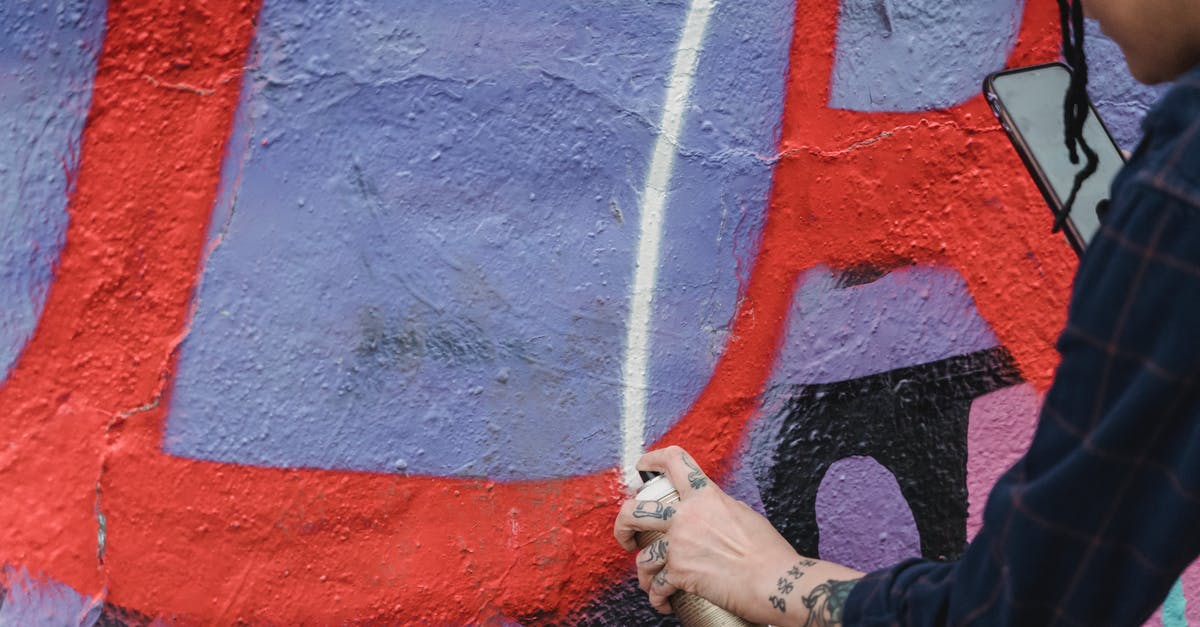 How can Malekith create the Aether? - Side view of crop unrecognizable painter spraying paint on colorful wall with patterns while creating graffiti on street of city