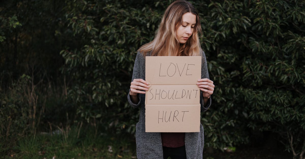 How can Neo stand a chance against Bane? - Lonely upset female in casual outfit standing near trees and grass while holding cardboard against abuse with inscription Love Should Not Hurt