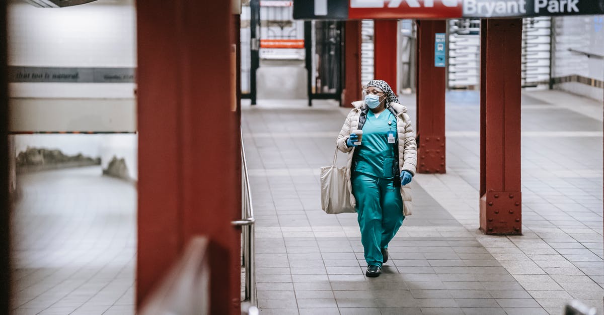 How can they walk normally in the space station? - Full body of female in medical uniform protective mask and gloves walking on subway station in New York with paper cup and fabric bag