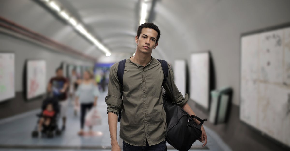 How can they walk normally in the space station? - Calm young African American male in casual clothes with big black bag and backpack looking at camera while walking along corridor of underground station against blurred passengers