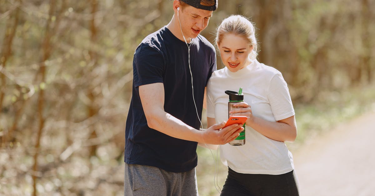 How could Carl run or jump when he is using apparatus for his walking? - Young man in earbuds sharing cellphone with young woman drinking water from plastic bottle during workout in nature together