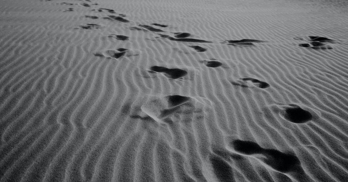 How deep is the hole in Sparta - Black and white of rows of footprints on empty wavy sandy shore in daytime