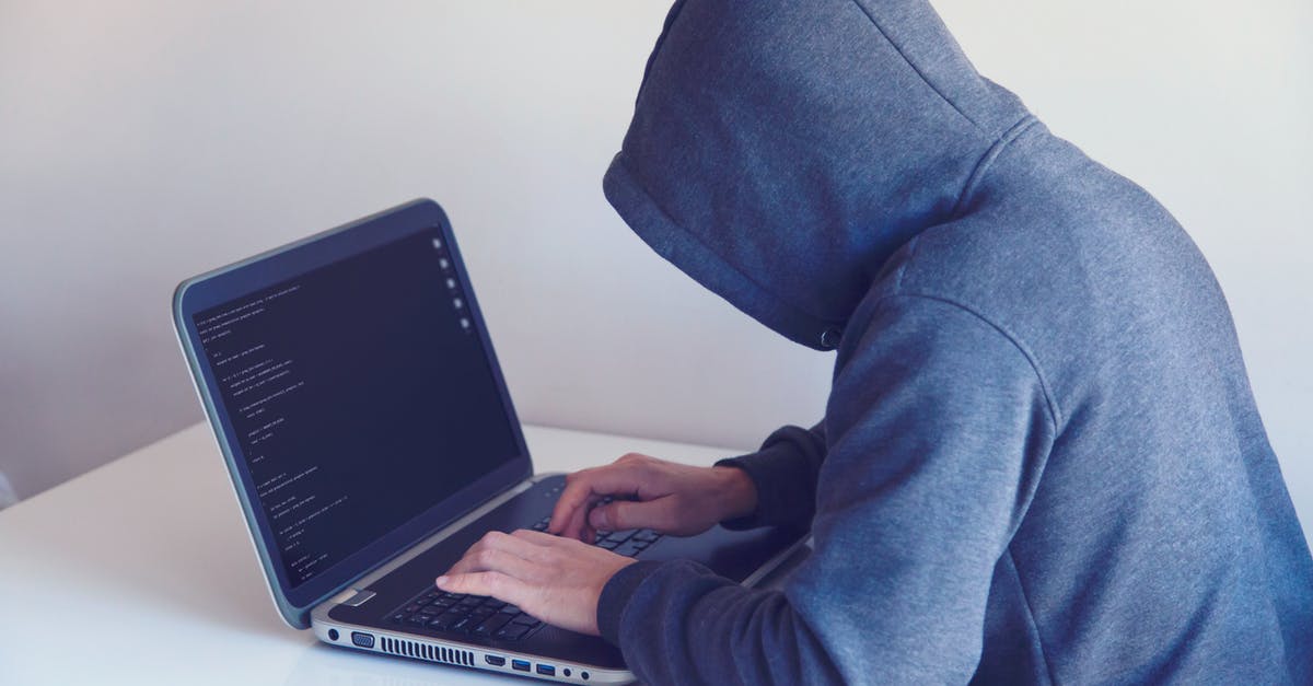 How did Finch's cover identity get blown? - Side view of unrecognizable hacker in hoodie sitting at white table and working remotely on netbook in light room near wall