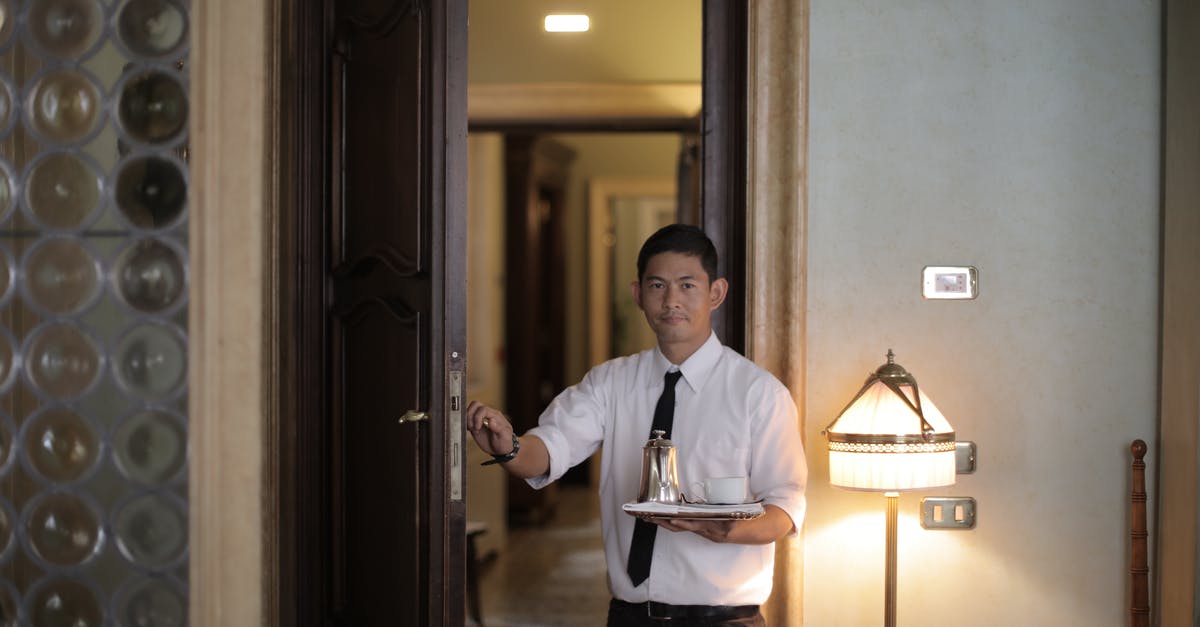 How did he enter the locked room? - Friendly ethnic male waiter serving clients in room and carrying tray with coffee while working in stylish hotel