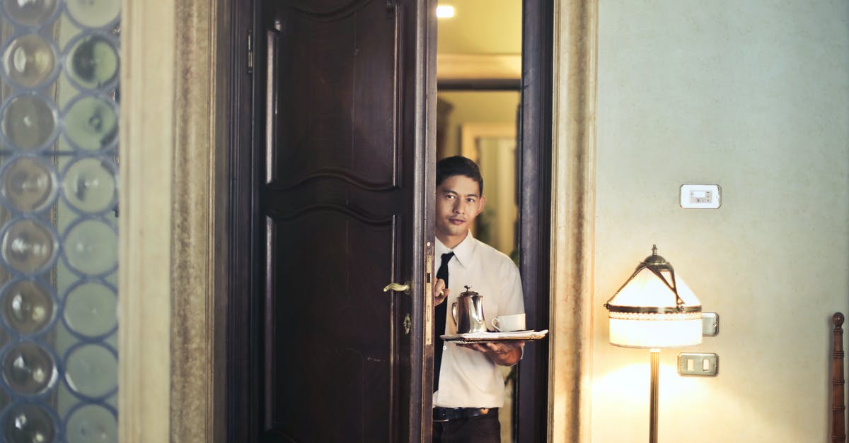 How did he enter the locked room? - Young ethnic male room service waiter carrying tray with coffee pot while entering hotel room with stylish vintage interior
