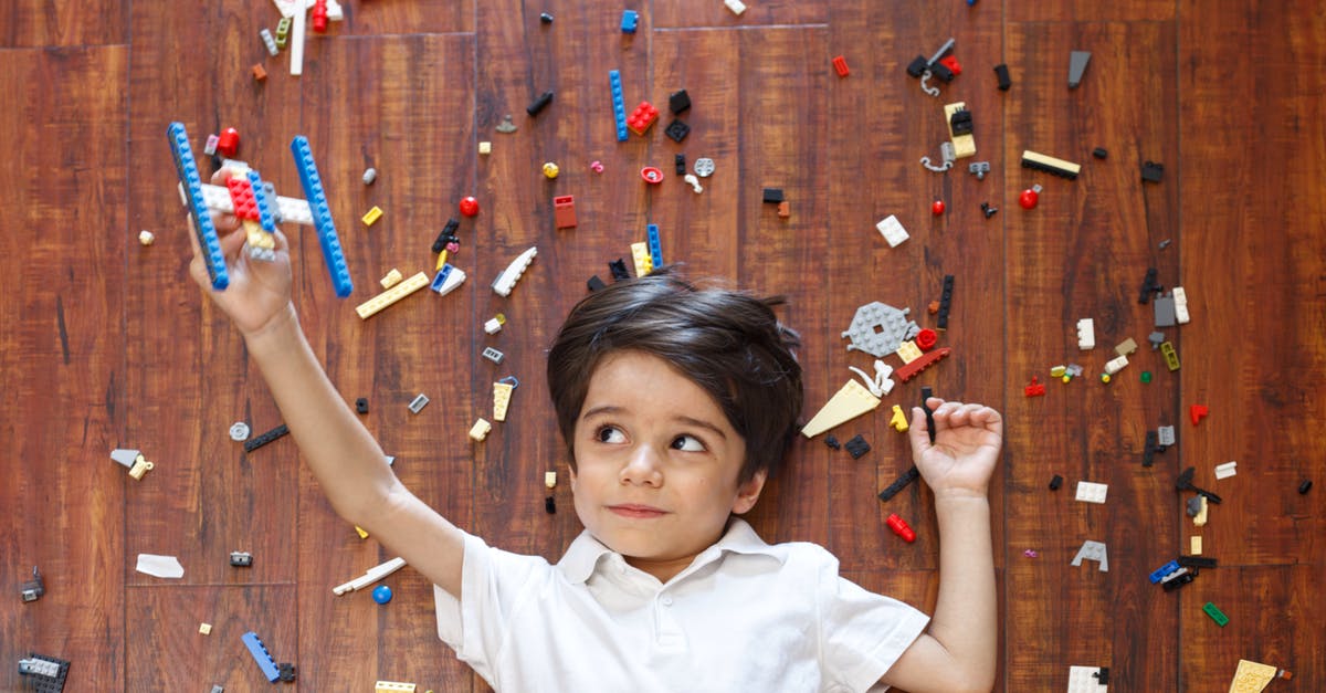 How did he set up time bomb? - Top view of concentrated kid lying on floor among various details of construction set while playing with handmade airplane