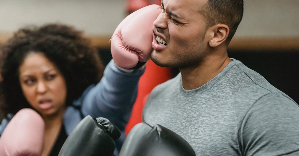 How did Ron get hurt so much when the Queen attacked his horse? - Side view of young muscular ethnic male trainer in sportswear and boxing gloves receiving heavy punch on face from serious young African American female during workout