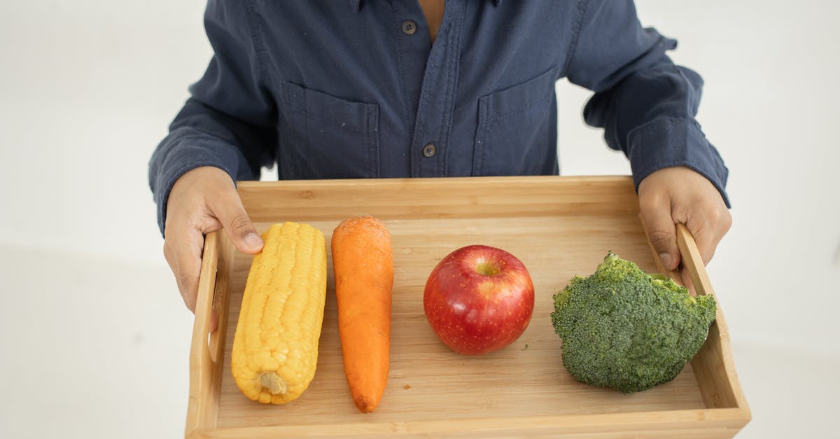 How Did the Children of the Corn Manage For So Long? - From above of crop anonymous kid in casual outfit holding wooden tray with fresh healthy broccoli apple carrot and corn against white background