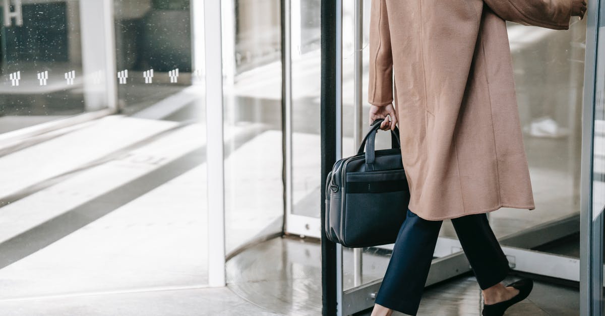 How did the lady with the revolver see the hollow? - Back view of crop stylish female manager in elegant clothes with briefcase in hand entering modern building through revolving door while going to work