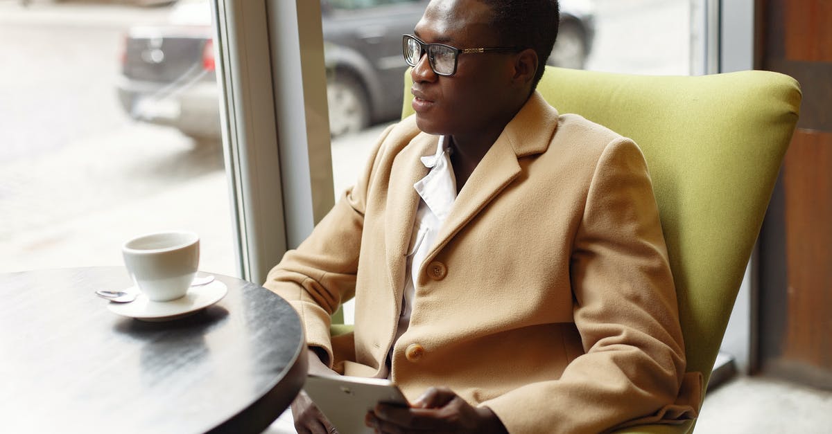 How did the watch do what it did? - Serious African American male in trendy formal suit and eyeglasses sitting on cozy chair in cafe with cup of coffee and browsing tablet