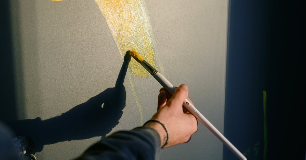 How did they create The Shadow's disguise? - Unrecognizable professional male painter drawing yellow gouache with paintbrush in sunlight while casting shadow on black wall while creating artwork