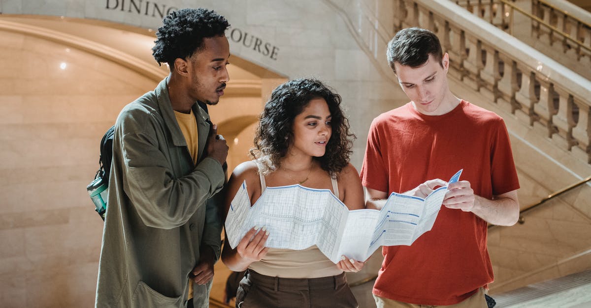 How did they find the location of Panda village? - Focused young man pointing at map while searching for route with multiracial friends in Grand Central Terminal during trip in New York