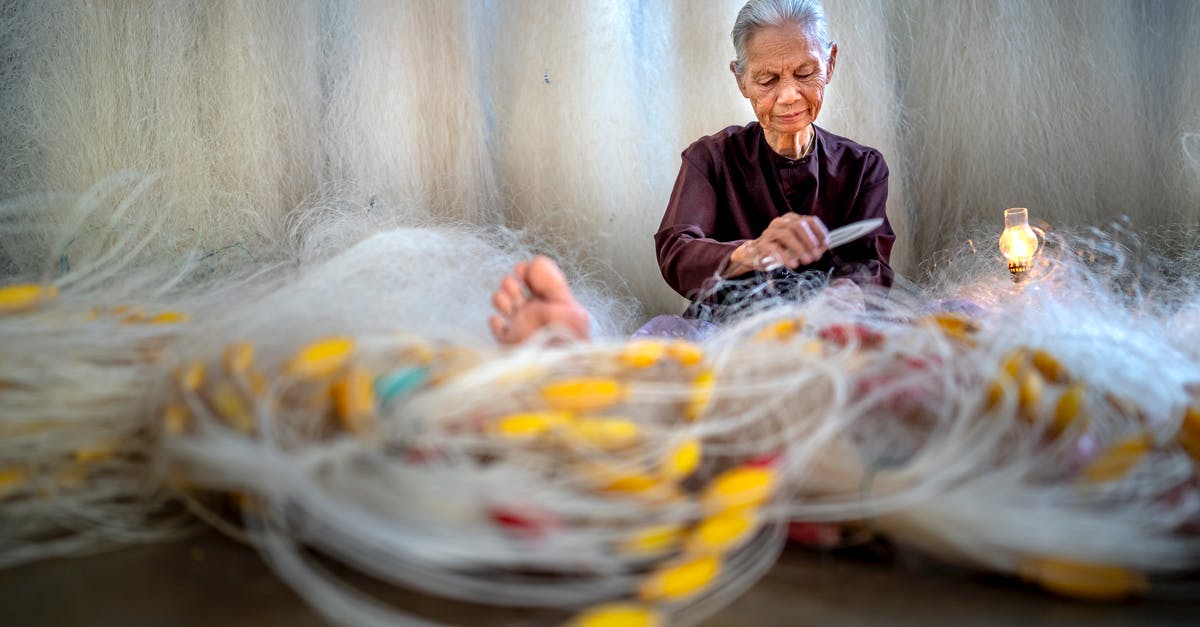 How did they make Yogurt so short? - Elderly Asian woman repairing fishing net against lamp