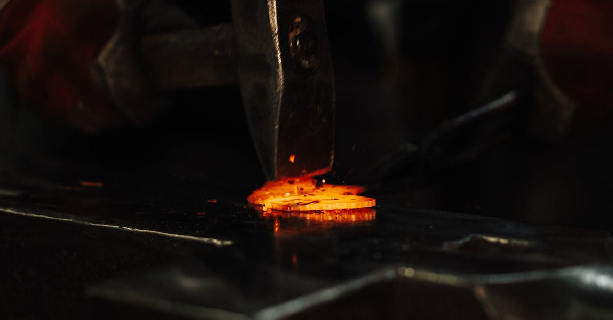 How did Tony fix himself by the end of Iron Man 3? - High angle of crop anonymous male blacksmith using hammer while forging metal detail in workshop