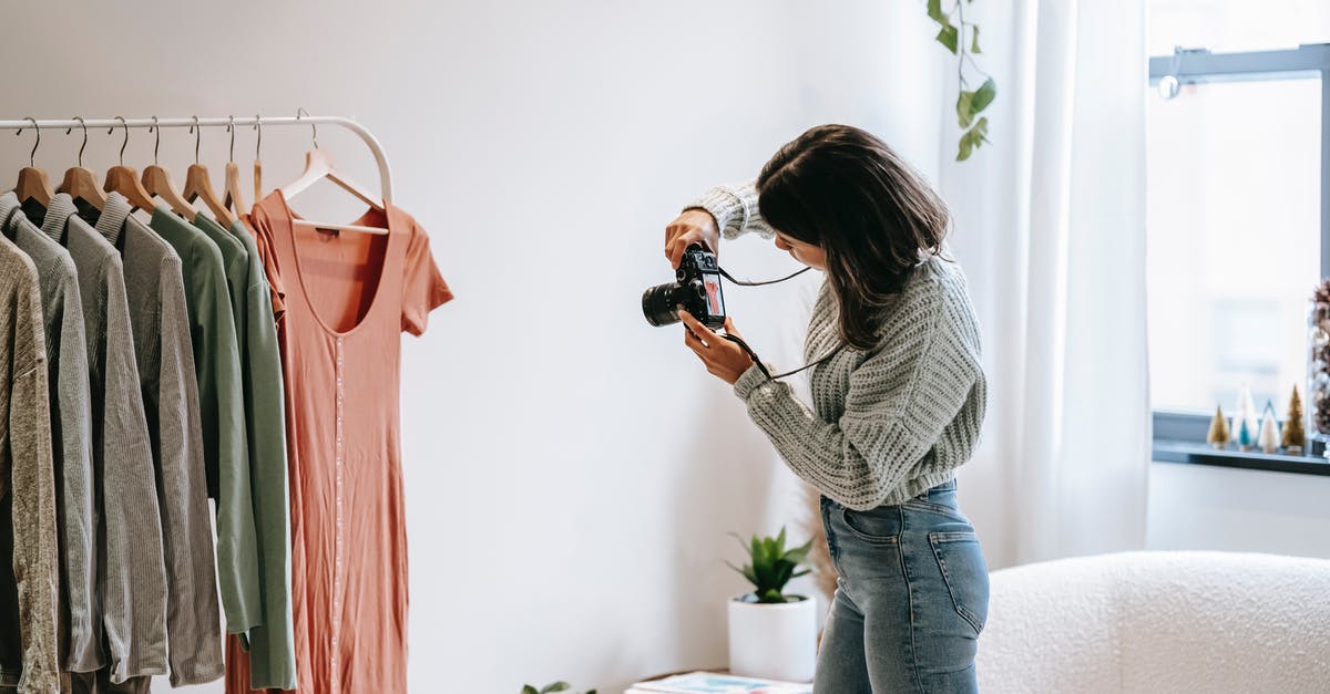 How do live studio audiences work when sitcoms can have multiple takes? - Side view of young female photographer in casual outfit standing in front of hanger and taking picture with camera of shirt in modern apartment