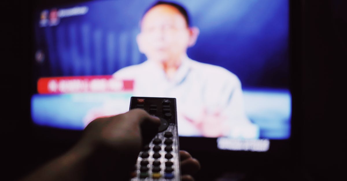 How do movie makers get people to watch a movie many times? - Crop anonymous person with remote controller switching channels while watching TV on blurred background in living room with dim light