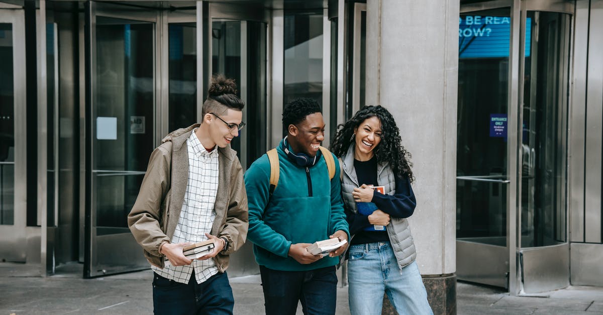 How do Mr. Brooks and Marshall have a conversation without alerting the surrounding people? - Young cheerful multiethnic students with books having fun on urban pavement while speaking in daylight