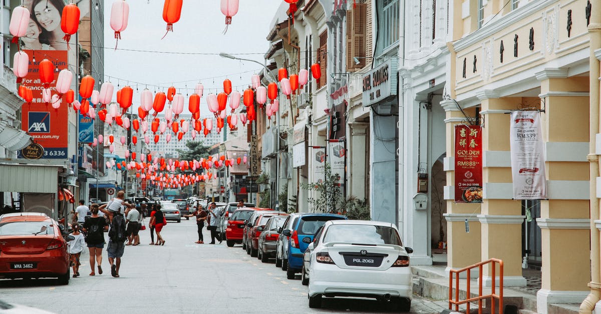 How do rashes relate to chinese cars? - Crowd of people strolling on asphalt road with parked cars on street with residential buildings and hanging Chinese lanterns in city