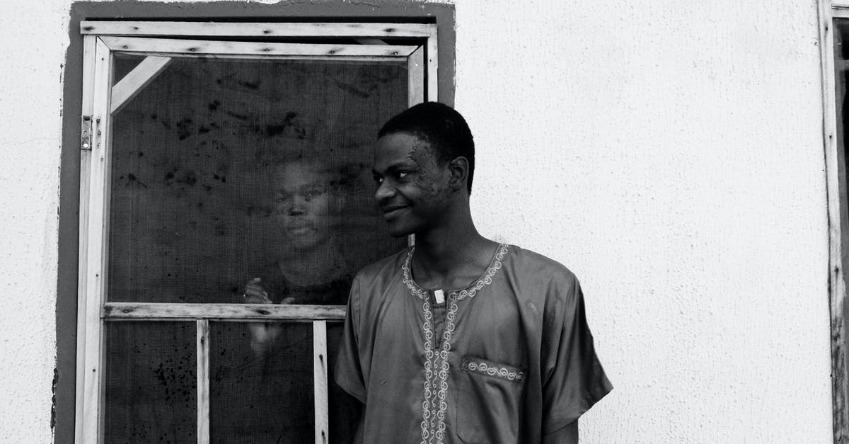 How do the characters' ages fit together in Blood & Chocolate? - Black and white of slim happy African American guy looking away while standing near house with concrete walls and old window with serious partner inside building