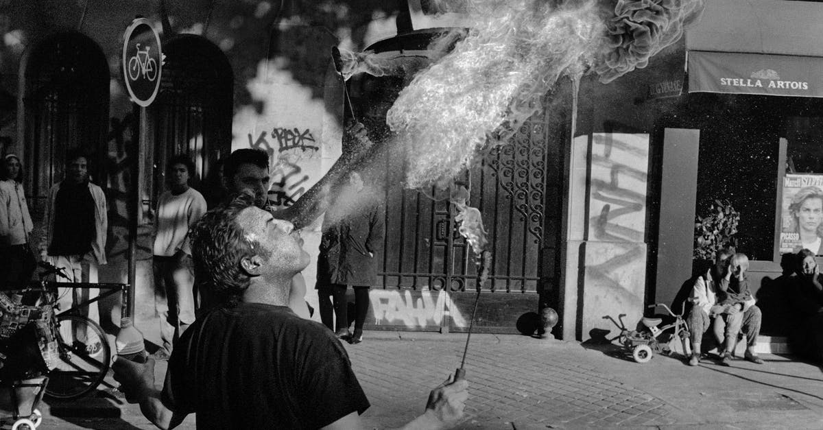 How do they film minors smoking? - Black and white of confident male acrobat blowing fire during show on city street