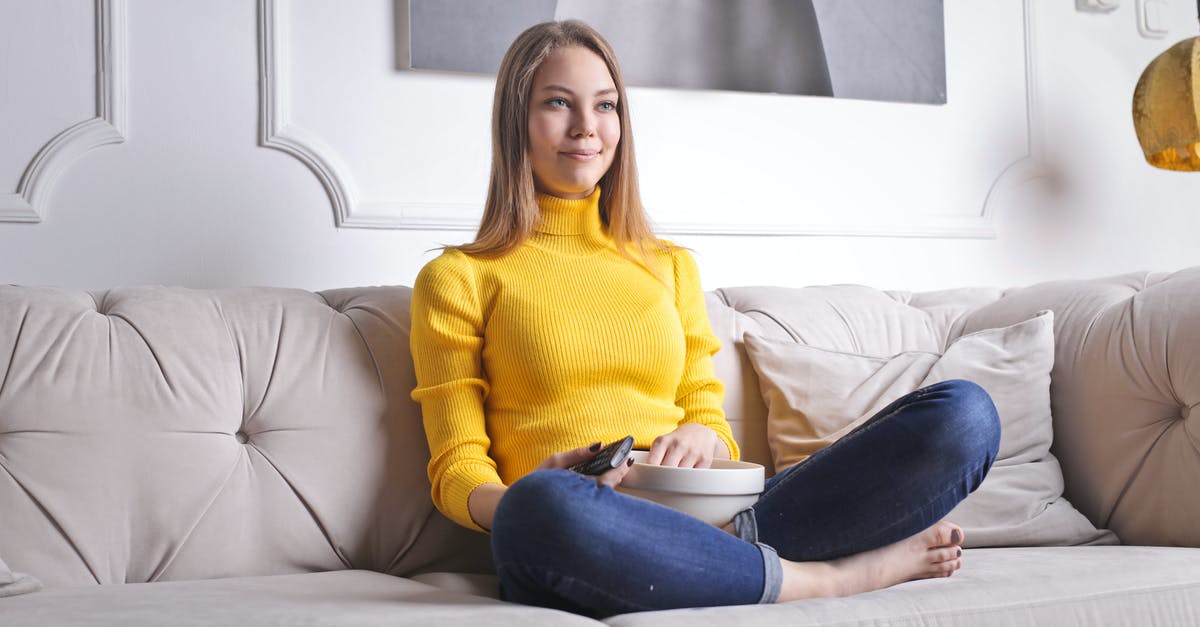 How do they film money in TV or movie? - Positive young female in casual clothes sitting on cozy sofa with bowl of snacks and watching interesting film while spending time at home