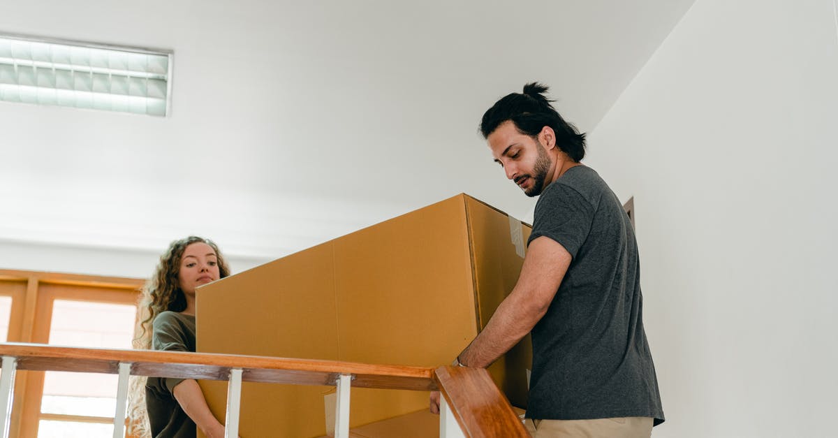 How do they remove the wires from flying/stunt scenes? - From below of couple in casual clothes carrying big carton box together while moving packed personal items into new apartment