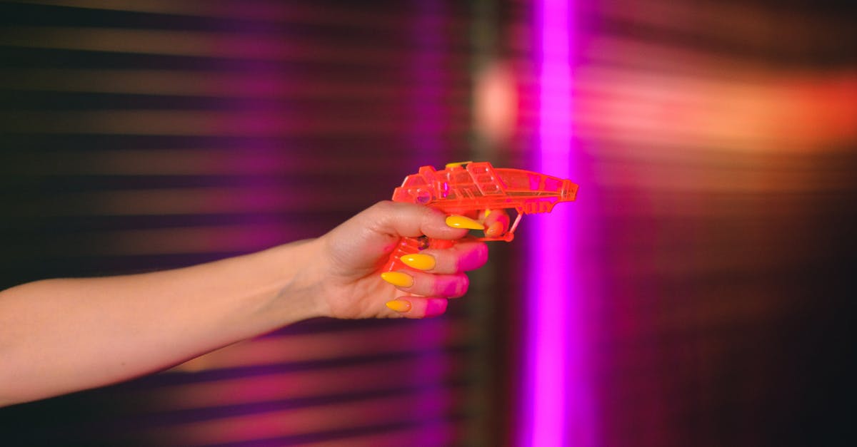 How do they shoot fight scenes without causing harm to performers? - Crop anonymous female with manicured hand pointing toy gun against neon lights in dark studio