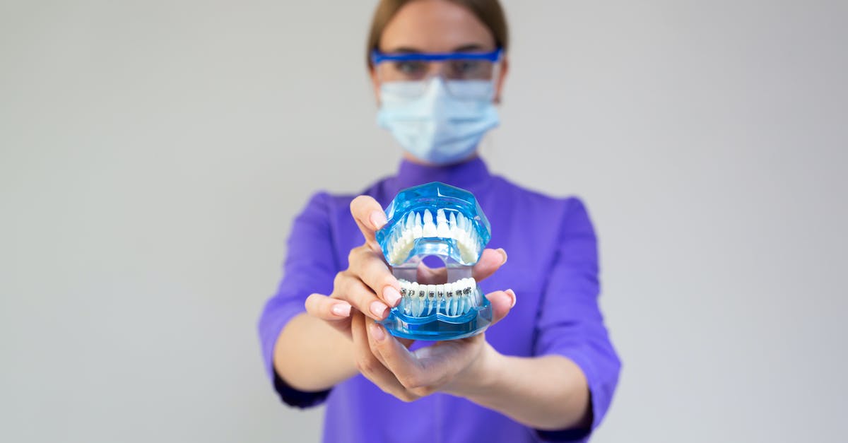How do they show a tooth-less mouth? - Female dentist in medical mask and protective eyeglasses demonstrating dental cleaning system with braces