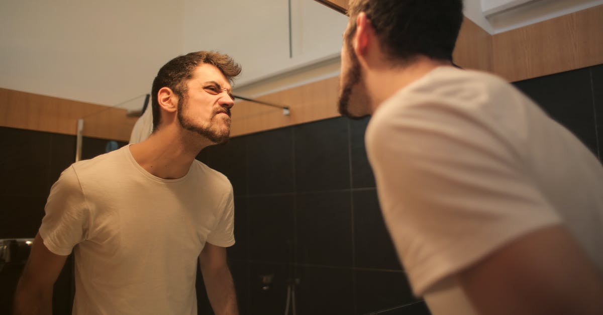 How does Doc Ock stay awake after being punched by Spider-Man? - Low angle side view of young bearded male in casual shirt standing in bathroom and looking at with frown mirror in morning