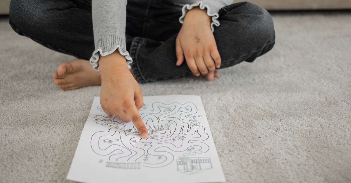 How does Dolores pass the test? - Crop anonymous barefooted child sitting on floor with crossed legs and solving labyrinth puzzle at home