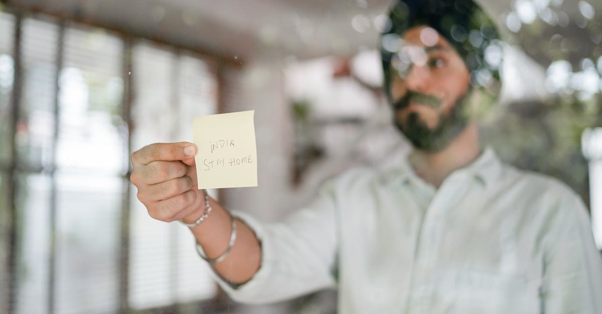 How does Guy know the world is ending? - Indian guy in turban and shirt with curled mustache sticking paper with INDIA STAY HOME inscription while standing behind glass wall during COVID 19 pandemic