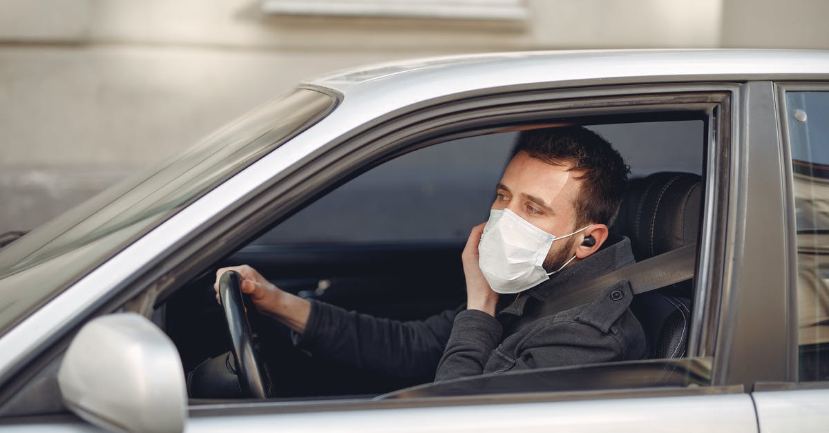 How does Guy know the world is ending? - Serious bearded male driver wearing warm jacket and protective facial mask using wireless earphones sitting in auto with opened window during coronavirus pandemic