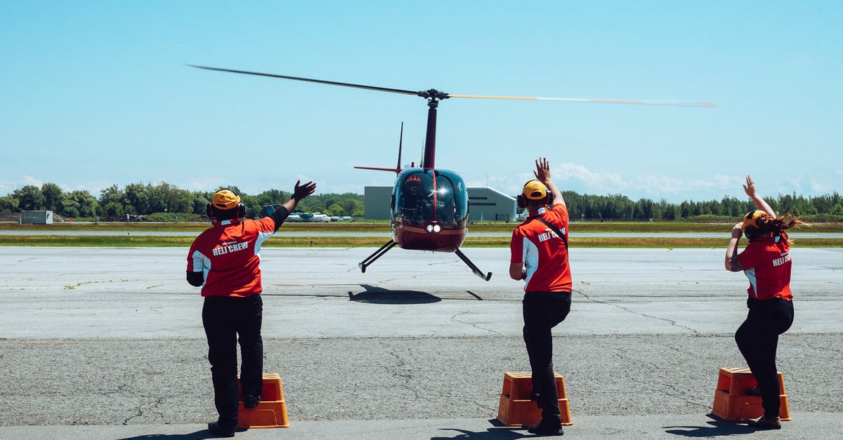 How does the crew of the SoL coordinate their lines in the theater? - Back view of anonymous ground crews in uniforms and headsets meeting passenger helicopter on airfield after flight against cloudless blue sky