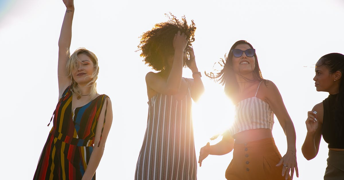 How does the escaping criminal move the fridge back? - From below of young content diverse ladies in trendy outfits smiling and dancing against cloudless sky during open air party on sunny day