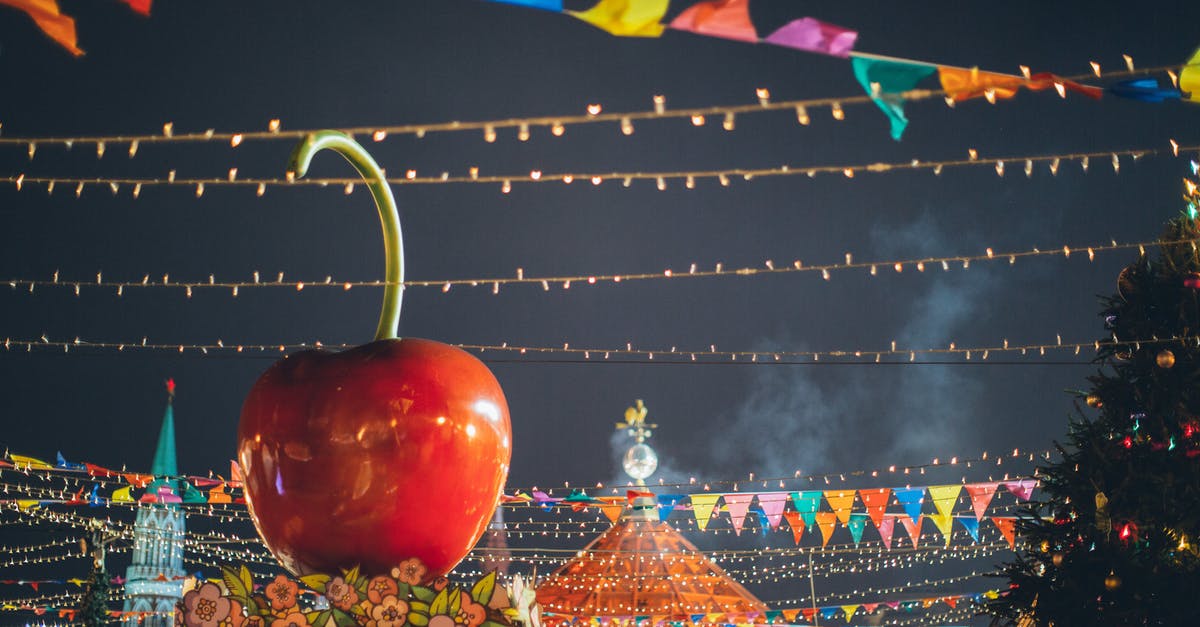 How does Timmy get fairies in Fairly OddParents? - Big red glossy toy apple on roof of building on fairground against dark sky in evening city park decorated to winter holidays