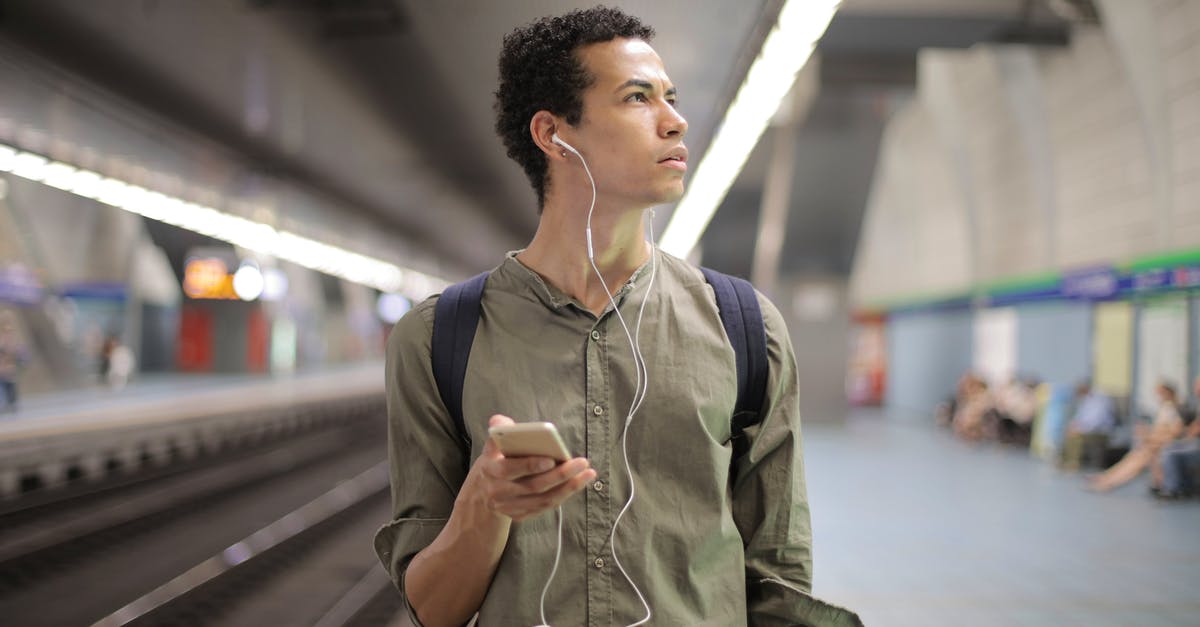 How is Agent J able to get the time-travel device in Men in Black 3? - Young ethnic man in earbuds listening to music while waiting for transport at contemporary subway station