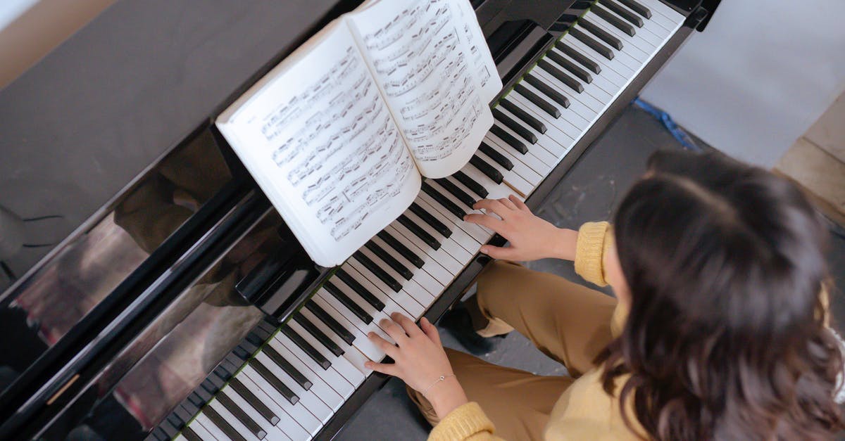 How is David playing a melody from an out-of-universe soundtrack? - From above of crop faceless woman in warm yellow sweater with music book practicing music on piano in light classroom