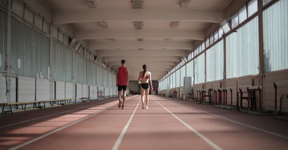 How long were John and Jane together for in Predestination? - Back view of sportsman and sportswoman in activewear walking along running track in athletics arena during warming up before training