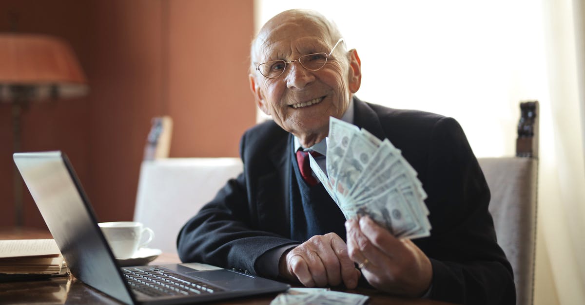 How much does Alicia earn? - Happy senior businessman holding money in hand while working on laptop at table