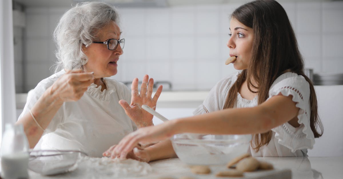 How old is Mike's granddaughter? - Calm senior woman and teenage girl in casual clothes looking at each other and talking while eating cookies and cooking pastry in contemporary kitchen at home