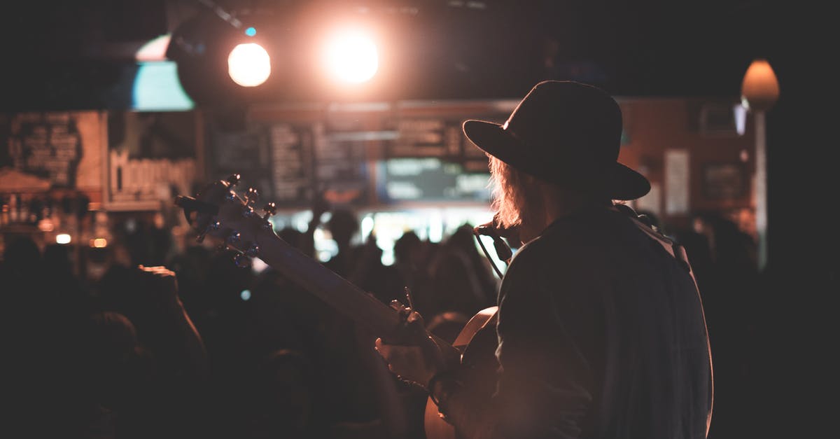 How the audience does not notice voice difference when "singing-voice" dubbing? [closed] - Back view of anonymous male artist playing acoustic guitar and singing song on stage during concert in dark club