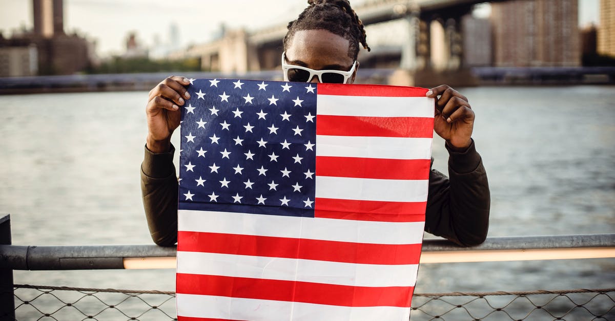 How was Coming to America received in the black community? - Ethnic male in casual clothes and sunglasses standing on embankment of city river while leaning on fence showing national flag of United States of America