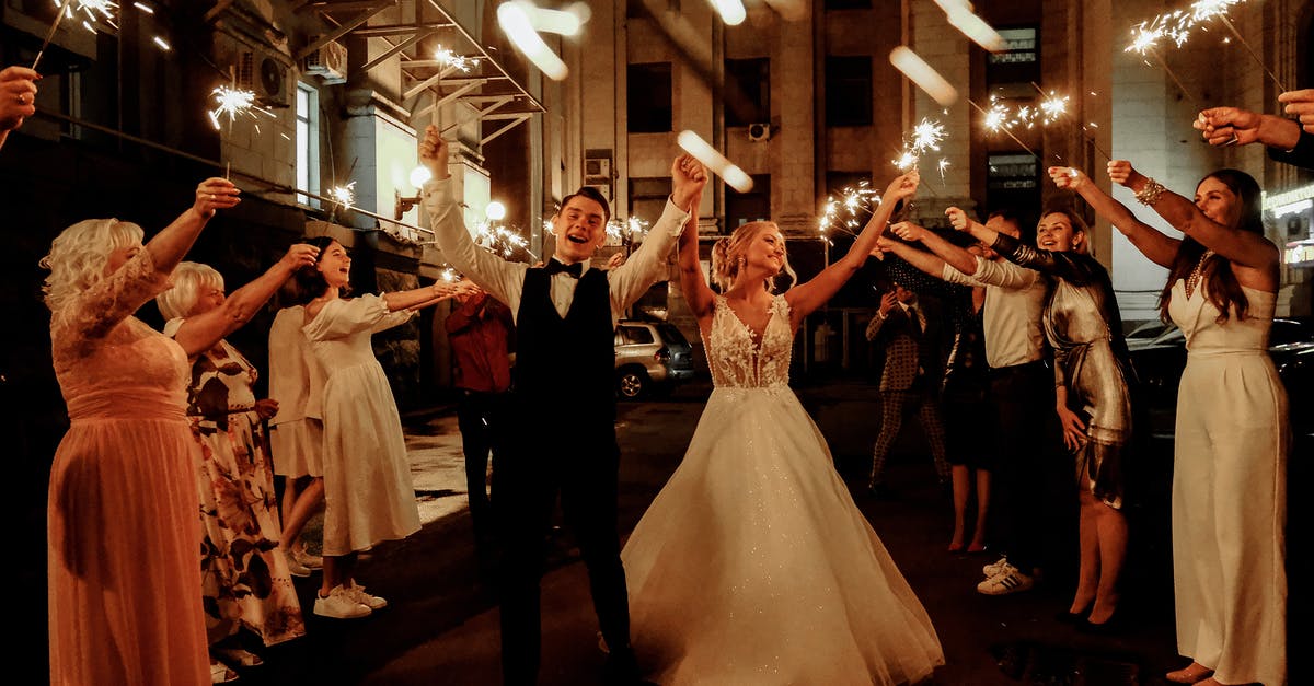 How was Deke Simmons married to Mimi Corcoran - Cheerful young bride and groom with guests dancing on street with sparklers in hands during wedding party